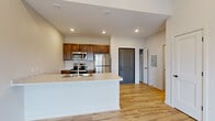 Located at 1220 W Highland Blvd in Lincoln, Nebraska, this thoughtfully designed one-bedroom, one-bathroom unit offers a compact yet functional living experience across a single floor. The open-concept layout connects the kitchen and living area seamlessly, creating a sense of spaciousness throughout. Light-toned hardwood-style flooring runs continuously through the space, complementing the crisp white walls and recessed lighting above.

The kitchen is a standout feature, anchored by a peninsula with a light stone-look countertop, an integrated sink, and dark walnut-toned cabinetry. A full suite of stainless steel appliances — including a refrigerator, electric range, microwave, and dishwasher — adds a modern, polished finish. The living area benefits from vaulted ceilings and a sliding glass door that opens to a private balcony, allowing natural light to pour in and offering open outdoor views.

The bedroom is a well-proportioned, quiet retreat with large windows, a wall-unit HVAC system, and continued hardwood-style flooring. A dedicated closet provides practical storage. The bathroom features a full tub-shower combination with chrome fixtures and a clean, minimalist design. The overall ambiance is fresh, modern, and move-in ready, ideal for those seeking a well-appointed home in Lincoln.