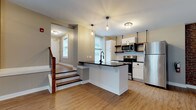 This single-floor space showcases a compelling mix of industrial character and contemporary updates throughout. Exposed red brick walls serve as a defining architectural feature across the main living areas, complemented by visible stainless steel ductwork running along the ceilings, lending an authentic loft-style aesthetic. Light wood-tone flooring flows through the open-plan living and kitchen areas, enhancing the sense of openness and continuity.

The kitchen is thoughtfully appointed with white cabinetry, dark granite countertops, stainless steel appliances including a refrigerator, range, and microwave, open wood shelving, and a central island with pendant lighting overhead. A staircase near the kitchen entry connects to additional levels. The entry foyer is compact yet functional, featuring wood flooring and a window for natural light.

The spacious main living area is lined with multiple windows set into the brick wall, allowing abundant natural light to fill the room. A sliding barn door adds a stylish transitional element between spaces. The bedroom features carpeted flooring and exposed brick with generous window placement. A secondary carpeted room with exposed ductwork offers flexible use. The bathroom includes a glass-enclosed shower with black framing, wood-look flooring, and clean neutral finishes throughout.