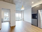 Located on the 8th floor at 5250 Rue Molson in Montreal, this modern one-bedroom, one-bathroom unit showcases an industrial-contemporary design highlighted by exposed concrete ceilings that contrast beautifully with crisp white walls and light hardwood flooring throughout. The open-concept living and kitchen area is bright and efficiently laid out, anchored by a stylish kitchen featuring matte charcoal lower cabinetry, white upper cabinets, a bold hexagonal tile backsplash, stainless steel appliances, and a peninsula island with a built-in sink — ideal for both cooking and casual dining. A geometric pendant light adds a designer touch overhead. The living area opens directly onto a private balcony through sliding glass doors, allowing natural light to pour in and offering open city views. The spacious bedroom includes an integrated built-in desk, exposed concrete ceiling details, and a window with outdoor views, providing a calm and functional retreat. A dedicated closet offers wire shelving for organized storage. The bathroom is finished with clean tile work, a glass shower enclosure, dark cabinetry for storage, and wood-toned flooring. An in-unit laundry area completes this well-appointed urban home.