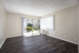 Located along Sylvan River in Fountain Valley, CA, this single-story unit offers a functional and well-maintained layout suited for comfortable living. The kitchen is a notable highlight, featuring white cabinetry with crown molding detail, granite-look countertops, recessed lighting, a double stainless steel sink, a white electric coil range with overhead ventilation, a dishwasher, and a tall pantry-style cabinet providing generous storage. Wood-look vinyl flooring runs throughout the kitchen and common areas, lending a cohesive, clean aesthetic.

The living area is bright and open, benefiting from a large sliding glass door with vertical blinds that opens to an outdoor patio, allowing abundant natural light to fill the space. A wall-mounted HVAC unit is also present. The textured ceilings are consistent throughout the living and bedroom spaces.

The bedrooms are carpeted and well-sized, with neutral warm-toned walls. The primary bedroom includes a walk-in closet and a window overlooking greenery outside. Additional bedrooms feature access to hallway spaces and wall vents for climate control.

The bathroom is clean and simply appointed, with a tub-shower combination, white fixtures, a vanity with a light countertop, and wood-look flooring.
