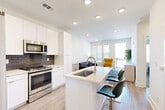 This thoughtfully designed one-bedroom, one-bathroom residence delivers a clean, contemporary aesthetic across a single floor. The open-concept kitchen flows seamlessly into the living area, anchored by a large island with a built-in sink, light quartz countertops, and bar seating for casual dining. The kitchen is outfitted with stainless steel appliances — including a refrigerator, range, microwave, and dishwasher — complemented by crisp white cabinetry and a navy blue subway tile backsplash. Light wood-look flooring ties the kitchen and living spaces together. The living room is bright and welcoming, featuring large windows with blinds that allow generous natural light, and a door leading out to a private balcony. The bedroom offers comfortable carpeting, a ceiling fan, and dual windows with urban views, creating a calm retreat. Adjacent to the bedroom is a well-appointed bathroom with wood-look tile flooring and a walk-in closet with built-in shelving that provides ample, organized storage. Throughout, the residence maintains a neutral, modern palette with recessed lighting, clean lines, and a cohesive design that maximizes the efficient use of space.