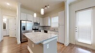 Located at 2920 W El Dorado Blvd in Friendswood, Texas, this single-story residence offers a well-designed layout with modern finishes throughout. The open-concept kitchen serves as a central highlight, featuring crisp white cabinetry, granite countertops, a central island with pendant lighting, and a full suite of stainless steel appliances including a French door refrigerator, range, microwave, and dishwasher. A tile backsplash and wood-look flooring complete the polished look. The living area is bright and airy, with large windows allowing ample natural light and a ceiling fan overhead. Crown molding adds a refined architectural touch throughout. Bedrooms are finished with plush carpeting, offering a comfortable retreat, while the carpeted walk-in closet provides generous storage with built-in shelving and hanging rods. The primary bathroom is well-appointed with dual granite-topped vanities, a glass-enclosed walk-in shower, wood-look flooring, and a large mirror. The entryway opens into a welcoming foyer with hardwood-style flooring and clean white walls, setting a neutral, move-in-ready tone. Overall, the space balances functional design with contemporary finishes in a clean, light-filled environment.