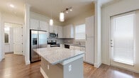 Located at 2920 W El Dorado Blvd in Friendswood, Texas, this single-story residence offers a well-designed layout with modern finishes throughout. The open-concept kitchen serves as a central highlight, featuring crisp white cabinetry, granite countertops, a central island with pendant lighting, and a full suite of stainless steel appliances including a French door refrigerator, range, microwave, and dishwasher. A tile backsplash and wood-look flooring complete the polished look. The living area is bright and airy, with large windows allowing ample natural light and a ceiling fan overhead. Crown molding adds a refined architectural touch throughout. Bedrooms are finished with plush carpeting, offering a comfortable retreat, while the carpeted walk-in closet provides generous storage with built-in shelving and hanging rods. The primary bathroom is well-appointed with dual granite-topped vanities, a glass-enclosed walk-in shower, wood-look flooring, and a large mirror. The entryway opens into a welcoming foyer with hardwood-style flooring and clean white walls, setting a neutral, move-in-ready tone. Overall, the space balances functional design with contemporary finishes in a clean, light-filled environment.
