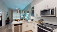This single-floor residence is designed with a contemporary aesthetic, combining functional layout with modern finishes. The open-concept kitchen is a standout feature, equipped with stainless steel appliances including a range, microwave, and dishwasher, complemented by white shaker cabinetry, granite countertops, and a subway tile backsplash. A peninsula with an undermount sink serves as the kitchen's focal point, illuminated by a trio of brushed gold pendant lights that extend into the adjoining living area. The vaulted ceiling height in this shared space enhances the sense of openness, while a ceiling fan provides added comfort.

The living area features soft sage-green walls, large windows with blinds and curtain panels that allow ample natural light, and wood-look flooring that runs throughout the main spaces. The bedroom is carpeted and offers a tranquil retreat, featuring French doors, a sliding barn door, and access to a generously sized walk-in closet with built-in wire shelving. The bathroom is outfitted with a white vanity, granite countertop, a large mirror with overhead lighting, and wood-look flooring that ties cohesively to the rest of the home.
