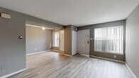 This two-floor residence is finished with a consistent palette of grey-toned walls and light wood-look vinyl plank flooring that extends throughout both levels, creating a cohesive and low-maintenance interior. The entry level opens into a living area that receives natural light through windows dressed with vertical blinds. A staircase with white railings connects the floors, and an interior door on the main level provides access to additional storage or utility space.

The galley-style kitchen runs along parallel walls and is equipped with white cabinetry, dark granite-style countertops, a stainless steel sink, a black refrigerator, and a white range with overhead cabinetry. The efficient layout maximizes storage and workspace within a compact footprint.

The bathroom features light wood-look flooring, a white vanity with a mirror above, a toilet, a towel bar, and a tub-shower combination with white tile surround.

The bedrooms, located on the upper level, are generously proportioned rooms with neutral grey walls, light flooring, and individual closets. Several bedrooms feature windows that allow natural light to filter in, and at least one bedroom is positioned adjacent to the bathroom for added convenience. The overall design is practical and consistent throughout.