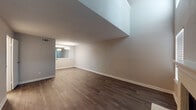 This two-story space offers a thoughtfully designed layout that balances open living areas with private upper-level rooms. The main floor is anchored by a spacious living area finished with rich, dark hardwood-style flooring that extends throughout. A tiled fireplace with a clean, light-colored surround serves as a focal point, complemented by a front entry door and window that bring in natural light. The vaulted ceiling area creates an open, airy atmosphere, with the upper level visually accessible from below, adding architectural depth to the main living space.

The kitchen is configured in a galley style and features white cabinetry with brushed nickel hardware, a herringbone-patterned tile backsplash, quartz-style countertops, black appliances including an electric range and refrigerator, and a standout farmhouse-style sink with a pot-filler faucet. A dining area adjacent to the kitchen is accented with a pendant light fixture and mirror.

The bathroom on the main level includes a white vanity with a quartz countertop, framed mirror, and a full tub-shower combination with white tile surround, set on dark hardwood-style flooring.

Upstairs, the bedrooms feature plush carpeting and are bathed in natural light through windows, with one room showcasing interior clerestory-style windows overlooking the lower level, enhancing the open, connected feel of the home.