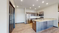 This single-floor unit offers a thoughtfully designed layout with contemporary finishes throughout. The open-concept kitchen serves as the centerpiece, anchored by a peninsula-style island with granite countertops and an undermount sink. Dark-toned shaker-style cabinetry with black hardware lines the walls, complemented by matching granite surfaces and a full suite of stainless steel appliances, including a French door refrigerator, electric range, and built-in microwave. Recessed lighting illuminates the kitchen and adjoining living area, which features light-toned hardwood-style flooring that extends throughout the main living spaces.

The bedrooms are carpeted and receive generous natural light through large, boldly framed windows with views of the surrounding neighborhood. Each bedroom includes a ceiling fan or baseboard heating unit, providing year-round comfort. A dedicated laundry area with a stacked washer and dryer adds practical convenience.

The bathroom is well-appointed with granite vanity countertops, a dark shaker-style cabinet base, a large mirror, and a full tub-shower combination. Consistent finishes—including brushed nickel fixtures and wood-look flooring—tie the space together for a cohesive, modern aesthetic throughout.