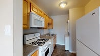 This single-floor residence offers a practical and comfortable layout designed for everyday living. The kitchen is efficiently arranged with warm honey-toned wood cabinetry, granite-look countertops, and durable dark tile flooring. It is equipped with a full suite of white appliances, including a gas range, over-the-range microwave, dishwasher, and refrigerator. A stacked washer and dryer unit is conveniently tucked within the kitchen area, adding in-unit laundry functionality.

The living area is generously proportioned, featuring neutral-toned carpet and a sliding glass door dressed with vertical blinds that invites natural light and provides access to an outdoor space. A ceiling fan enhances comfort throughout the open layout, which flows into an adjacent dining or secondary living area.

The bedrooms are well-sized and carpeted, finished in soft neutral tones that create a calm and restful atmosphere. One bedroom benefits from a window with views of surrounding greenery, allowing natural light to fill the room.

The bathroom is clean and straightforward, featuring warm terracotta-toned tile flooring, a tub-shower combination with a curtain rod, a toilet, and a white vanity. The overall design of this residence prioritizes functionality and comfortable, move-in ready living.