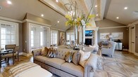 Located at 20 Ashton Village Dr in Westerville, Ohio, this single-floor space exudes sophistication and refined elegance at every turn. The main living area commands attention with its soaring vaulted ceilings adorned with decorative exposed beams, creating a sense of grandeur and openness. A striking geometric chandelier serves as a dramatic focal point, complementing the airy, light-filled atmosphere cultivated by an abundance of recessed lighting and large French doors that invite natural light deep into the interior. The stone-accented fireplace anchors the room with warmth and texture, flanked by classic columned detailing that adds a timeless architectural character. Neutral tones in warm greige and cream run throughout, lending the space a cohesive and inviting ambiance. The living area is generously proportioned, comfortably accommodating substantial furnishings while maintaining a sense of ease and flow. French doors along the walls hint at seamless transitions between interior zones, suggesting a thoughtfully designed layout that balances openness with defined spaces. The overall aesthetic blends traditional architectural elements with contemporary styling, resulting in a space that is both impressive in scale and welcoming in character.