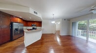 Located at 6116 Yellow Sun Drive in Lantana, FL, this single-story, three-bedroom, two-bathroom home offers a well-designed open-concept layout with a warm and cohesive aesthetic throughout. Rich hardwood flooring flows seamlessly across the main living areas, anchoring the space with a sense of warmth and continuity.

The kitchen is a standout feature, showcasing deep cherry wood cabinetry, granite-look countertops, and a full suite of stainless steel appliances including a refrigerator with ice maker, electric range, and built-in microwave. A peninsula breakfast bar connects the kitchen to the combined dining and living area, which is brightened by a pendant light fixture and offers a comfortable, open feel.

The three bedrooms are finished with the same hardwood flooring and feature clean white walls, offering a neutral canvas. One bedroom includes double doors and hallway access, while another benefits from a window with natural light. The primary bedroom provides a generous footprint with ample space.

The bathrooms include a tiled walk-in shower with glass doors and neutral stone-toned tile work. A dedicated laundry room houses a full-size washer and dryer with overhead shelving and additional cabinetry, adding everyday convenience. Two closets and two hallways round out the functional layout of this well-appointed home.