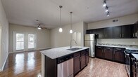 This single-story, 3-bedroom, 2-bathroom residence offers a thoughtfully designed layout that maximizes comfort and functionality. The open-concept kitchen and living area serves as the heart of the home, featuring rich hardwood-style flooring, a ceiling fan, and French doors that invite natural light and provide outdoor access. The kitchen is equipped with dark espresso cabinetry extending to the ceiling, granite countertops with a mosaic tile backsplash, stainless steel appliances including a refrigerator and dishwasher, and a central island with a built-in sink and pendant lighting overhead — ideal for both cooking and casual dining.

The two full bathrooms continue the cohesive design aesthetic with granite-topped dark vanities, large mirrors, and tiled tub-shower combinations accented with decorative mosaic borders. Each of the three bedrooms features plush carpeting, ceiling fans, and access to dedicated closet space; the walk-in closets are outfitted with wire shelving systems for organized storage. Neutral wall tones throughout lend a clean, versatile backdrop. Connecting hallways provide smooth circulation between the private and shared areas of the home, completing a well-balanced and move-in ready residence.