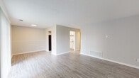 This single-floor residence in the Cambridge community of Louisville, Kentucky, offers a well-organized layout with a clean, neutral aesthetic throughout. The main living area is generously sized, featuring light gray wood-style flooring that extends seamlessly across the open space. Soft gray walls and a textured ceiling contribute to a bright, airy atmosphere. A central partial wall divides the living space while maintaining an open sightline to the kitchen beyond.

The kitchen is notably updated, showcasing crisp white cabinetry with brushed nickel hardware, light granite countertops, and black appliances including an electric range with overhead ventilation. Wood-style flooring continues here, complementing the modern finishes.

A separate room features a painted white brick accent wall alongside a sliding glass door fitted with vertical blinds, providing direct access to the outdoors and allowing natural light to enter.

The bedrooms are carpeted with plush neutral-toned carpet and each includes a ceiling fan with light fixture and a window with blinds for natural light and ventilation.

The bathroom is straightforwardly appointed with a full tub-shower combination, neutral walls, and standard fixtures. Overall, the space presents a functional, move-in-ready environment with consistent, updated finishes throughout.