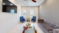 Located at 255 Fairview Rd in Henrietta, Texas, this single-story clubhouse offers a well-appointed community gathering space designed for both relaxation and functionality. Throughout the entire floor, polished marble-look tile flooring creates a clean, cohesive aesthetic that ties each room together seamlessly.

The entrance welcomes visitors into an open, bright layout. The living room is furnished with a tufted gray velvet sofa, bold blue wingback accent chairs, and a glass-top coffee table, all beneath a ceiling fan and recessed lighting — ideal for casual socializing or quiet downtime. A wall-mounted television adds to its versatility.

The adjoining dining area features a rustic wooden dining table surrounded by upholstered linen chairs with nailhead trim, bathed in natural light from large windows fitted with plantation-style blinds. A ceiling fan overhead ensures comfort year-round, and accessible restrooms are conveniently located nearby.

The kitchen is thoughtfully equipped with dark cabinetry, black granite countertops, a stainless steel refrigerator, microwave, double sink, water cooler, and pendant lighting. Tall windows flood the space with natural light, and soaring ceilings lend an airy, open feel.

Rounding out the clubhouse is a dedicated exercise room, providing residents with an on-site fitness option. The overall ambiance is modern, welcoming, and well-maintained.