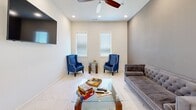 Located at 255 Fairview Rd in Henrietta, Texas, this single-story clubhouse offers a well-appointed community gathering space designed for both relaxation and functionality. Throughout the entire floor, polished marble-look tile flooring creates a clean, cohesive aesthetic that ties each room together seamlessly.

The entrance welcomes visitors into an open, bright layout. The living room is furnished with a tufted gray velvet sofa, bold blue wingback accent chairs, and a glass-top coffee table, all beneath a ceiling fan and recessed lighting — ideal for casual socializing or quiet downtime. A wall-mounted television adds to its versatility.

The adjoining dining area features a rustic wooden dining table surrounded by upholstered linen chairs with nailhead trim, bathed in natural light from large windows fitted with plantation-style blinds. A ceiling fan overhead ensures comfort year-round, and accessible restrooms are conveniently located nearby.

The kitchen is thoughtfully equipped with dark cabinetry, black granite countertops, a stainless steel refrigerator, microwave, double sink, water cooler, and pendant lighting. Tall windows flood the space with natural light, and soaring ceilings lend an airy, open feel.

Rounding out the clubhouse is a dedicated exercise room, providing residents with an on-site fitness option. The overall ambiance is modern, welcoming, and well-maintained.
