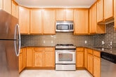 Located at 140 Mayhill St in Saddle Brook, NJ, this single-floor residence offers a thoughtfully designed layout with a clean, neutral aesthetic throughout. The open-concept living and dining area is highlighted by gleaming hardwood floors and recessed lighting, with a elegant pendant light fixture anchoring the space. This area flows seamlessly into the kitchen, which is outfitted with warm honey-toned wood cabinetry, granite countertops, a stylish subway tile backsplash, and stainless steel appliances including a gas range, microwave, and refrigerator. Tile flooring grounds the kitchen area. The bedrooms feature plush wall-to-wall carpeting and generous natural light from windows with outdoor views. The primary bedroom is complemented by a spacious walk-in closet with wire shelving systems offering ample storage. The en-suite primary bathroom includes a dual-sink vanity with wood cabinetry, tile flooring, and a glass-enclosed walk-in shower with tile surround. A second full bathroom features a tiled tub-shower combination and tile flooring. Throughout the residence, crisp white trim and neutral wall tones create a bright, welcoming ambiance well-suited for comfortable everyday living.