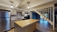 Located at 1503 Monmouth Avenue in Lancaster, Ohio, this two-floor home offers a thoughtfully updated interior with a cohesive modern design throughout. The kitchen serves as a standout feature, showcasing gray shaker-style cabinetry, granite countertops, and a mosaic tile backsplash in cool blue and gray tones. A large butcher block island anchors the space, providing ample prep and gathering room, while pendant lighting suspended from exposed beam detailing above adds an industrial-chic character. Stainless steel appliances, including a refrigerator, range, and dishwasher, complete the functional layout. Light wood-tone flooring runs through the main living areas, complementing the neutral gray palette used throughout the home. A staircase connects the two levels, with sliding glass door access visible from the kitchen area, bringing in natural light. The bathrooms feature gray cabinetry with granite-style countertops, light wood flooring, and a tub-shower combination. The bedrooms are carpeted in a soft gray tone and equipped with ceiling fans and natural light from windows overlooking greenery outside. The textured ceilings and consistent gray wall tones tie the entire home together with a clean, contemporary aesthetic.