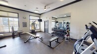 Located at 1 Springtime Blvd SW in Huntsville, Alabama, this fitness center offers a well-equipped, single-floor workout facility designed to support a comprehensive exercise routine. The space is finished with durable rubber flooring throughout, bold crown molding with dark trim accents, and crisp white walls that create a clean, professional atmosphere.

The strength training area is a focal point of the facility, featuring a full rack of dumbbells spanning a wide range of weights, a flat and adjustable weight bench, and a multi-functional cable machine ideal for a variety of resistance exercises. A large wall-mounted mirror expands the sense of space and allows users to monitor their form. A medicine ball rack and kettlebells round out the free weights section.

The cardio zone includes a treadmill and an elliptical machine, each equipped with individual display screens. Additional selectorized strength machines are positioned near large windows that invite natural light and provide outdoor views, contributing to an open and motivating environment. Wall-mounted televisions are placed throughout for entertainment during workouts.

A ceiling fan overhead aids in air circulation, while a standing scale and posted gym rules reflect an attentive, user-focused design. Multiple entry doors provide convenient access throughout the space, making this fitness center a fully functional and comfortable destination for daily exercise.