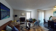 This single-floor residence offers a thoughtfully arranged layout that balances comfort and functionality across its key living spaces. The living room serves as a central gathering area, anchored by a white-mantled fireplace and adorned with a decorative sunburst mirror. Dark hardwood-style flooring runs throughout, providing a cohesive foundation, while a sliding glass door fitted with vertical blinds fills the space with natural light and offers outdoor access.

The galley-style kitchen is outfitted with dark cabinetry, white countertops, a subway tile backsplash, and black appliances including a range, microwave, and refrigerator. Track lighting and a window above the counter provide ample illumination. Adjacent to the kitchen, the dining area accommodates a round table with seating for four and features a pendant light overhead and a sliding glass door for additional natural light.

The bedroom is generously sized, featuring sliding glass door access to an outdoor patio, dark hardwood-style flooring, and textured walls. The bathroom includes a single-sink vanity with dark cabinetry, a large framed mirror, and a tub-shower combination with a decorative curtain. Neutral gray tones and textured ceilings are consistent throughout, contributing to a warm and cohesive ambiance.