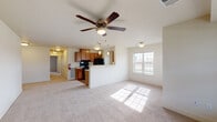 This single-floor residence is designed with an open, functional layout that seamlessly connects the main living areas. The spacious living room is finished with neutral-toned carpet and receives generous natural light through a large double-hung window. A ceiling fan with a built-in light fixture serves as a central feature overhead, contributing to both comfort and airflow throughout the space.

The kitchen opens directly to the living area via a half-wall peninsula, creating an accessible and social flow between the two spaces. It features warm-toned wooden cabinetry that extends to the upper walls for ample storage, black appliances including a range, refrigerator, and dishwasher, and light-colored countertops. Wood-look flooring runs throughout the kitchen, and a window above the counter brings in additional natural light.

The bedroom is generously proportioned with neutral carpet, crisp white walls, and a flush-mount light fixture. The full bathroom includes a tiled tub-and-shower combination, a wood-vanity with sink, hardwood-style flooring, and an adjacent walk-in closet with a shelf and hanging rod. A hallway with built-in storage connects the rooms, completing this well-organized and light-filled layout.