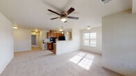 This single-floor residence is designed with an open, functional layout that seamlessly connects the main living areas. The spacious living room is finished with neutral-toned carpet and receives generous natural light through a large double-hung window. A ceiling fan with a built-in light fixture serves as a central feature overhead, contributing to both comfort and airflow throughout the space.

The kitchen opens directly to the living area via a half-wall peninsula, creating an accessible and social flow between the two spaces. It features warm-toned wooden cabinetry that extends to the upper walls for ample storage, black appliances including a range, refrigerator, and dishwasher, and light-colored countertops. Wood-look flooring runs throughout the kitchen, and a window above the counter brings in additional natural light.

The bedroom is generously proportioned with neutral carpet, crisp white walls, and a flush-mount light fixture. The full bathroom includes a tiled tub-and-shower combination, a wood-vanity with sink, hardwood-style flooring, and an adjacent walk-in closet with a shelf and hanging rod. A hallway with built-in storage connects the rooms, completing this well-organized and light-filled layout.