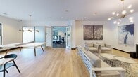 Located at 27 Station Ct in Greenville, South Carolina, this single-floor amenity space is thoughtfully designed to serve both fitness and social needs. The facility is divided into two distinct yet connected zones, seamlessly integrated through frosted glass sliding doors.

The fitness area is comprehensively outfitted with cardio equipment including treadmills, ellipticals, and a stationary bike, all positioned beneath a ceiling fan and large windows that bring in natural light and outdoor views. A dedicated strength and conditioning section features a multi-station cable machine, an organized dumbbell rack, medicine balls, stability balls, a weight bench, and a full wall of colorful exercise mats. A wall-mounted mirror expands the visual depth of the workout space, which is finished with durable rubber flooring.

The adjoining lounge area provides a welcoming retreat with warm hardwood flooring, white-painted brick walls, and recessed lighting. Comfortable woven lounge chairs and soft furnishings are arranged around a central area rug, while a large flat-screen TV mounted above a dark media console anchors one wall. Curated blue-toned artwork adds a sophisticated, cohesive aesthetic throughout. A dining-height table with pendant lighting provides an additional gathering spot, making this a versatile community space suited for both active and social use.
