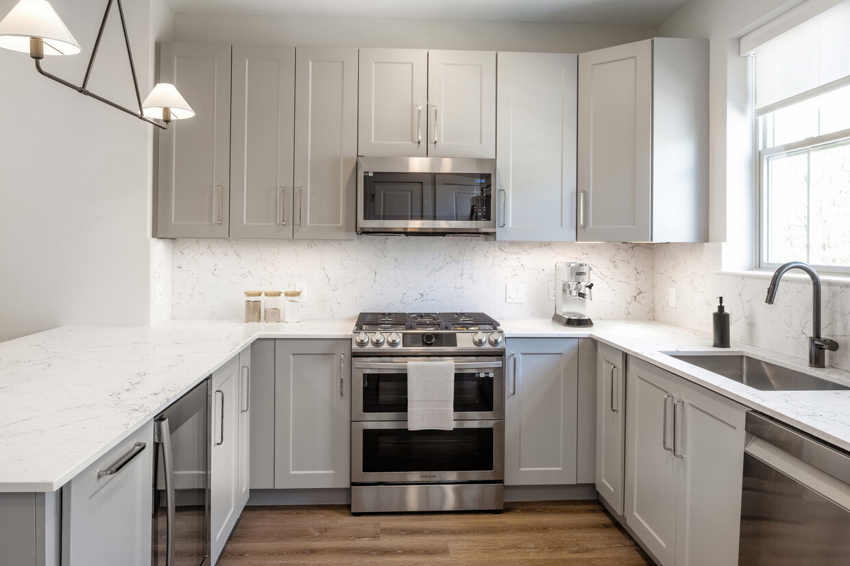 Signature Collection kitchen with stainless steel appliances, white quartz countertop, grey cabinetry, white quartz backsplash, and hard surface flooring - Avalon Princeton Circle