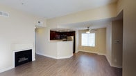 This single-level 2-bedroom, 1-bathroom residence offers a thoughtfully designed open-concept layout that maximizes comfort and functionality. The main living area features warm hardwood-style flooring that extends throughout the space, complemented by neutral, light-toned walls that create a bright and welcoming ambiance. A ceiling fan with a built-in light fixture anchors the living room, which also benefits from a window dressed with blinds that invites natural light while maintaining privacy. A fireplace adds a cozy focal point to the living area.

The kitchen is positioned centrally and defined by a curved breakfast bar that separates it from the main living space. Rich, dark-wood cabinetry pairs with stainless steel appliances, including a refrigerator and microwave, while recessed lighting overhead ensures the workspace is well-lit. The arched architectural passageway connecting the kitchen to the living area adds a refined design detail that enhances the overall aesthetic.

The layout is efficient and practical, with clearly defined spaces that flow naturally into one another. The combination of classic finishes, functional design, and carefully selected fixtures makes this residence a comfortable and stylish place to call home.