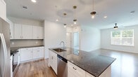 Located at 5617 Oakley Industrial Blvd in South Fulton, GA, this single-story residence offers two bedrooms and two bathrooms within a well-designed, efficiently laid-out floor plan. The open-concept kitchen and living area serves as the heart of the home, showcasing a large center island topped with dark granite countertops, a stainless steel undermount sink, and a stainless steel appliance suite including a French door refrigerator, range, microwave, and dishwasher. Crisp white shaker cabinetry, a subway tile backsplash, and Edison-style pendant lights suspended from brass fixtures contribute a contemporary yet warm aesthetic. Wood-look flooring runs throughout the main living areas, adding continuity and warmth. Both bedrooms feature plush carpeting and natural light from windows with outdoor views of surrounding greenery. The primary bedroom includes access to a dedicated closet and a private bathroom outfitted with granite vanity counters, tile flooring, and a tub-shower combination with white subway tile surround. The second bathroom mirrors this refined finish quality. Each bedroom benefits from its own closet, providing ample storage throughout the residence.