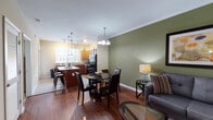 The Ashby presents a thoughtfully designed one-bedroom, one-bathroom residence in Chamblee, Georgia, offering a comfortable and functional single-floor layout. The open-concept living and dining area is anchored by rich hardwood flooring, crown molding, and an accent wall painted in a warm sage green, creating an inviting and cohesive aesthetic. A ceiling fan complements the living space, which flows naturally into the dining area illuminated by an elegant chandelier. The kitchen is well-equipped, featuring warm-toned cabinetry, tile flooring, a center island with pendant lighting, black appliances including a refrigerator, range, and microwave, plus a double sink beneath a bright window that fills the space with natural light. The bedroom offers plush carpeting, a tray ceiling, and a generous window dressed with layered curtains, providing a tranquil retreat. The full bathroom includes a soaking tub with tiled surround, white vanity cabinetry, and tile flooring. Throughout the residence, the design balances practicality with comfort, making this unit at 4306 N Shallowford Rd a well-rounded living space in the heart of Chamblee.