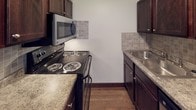This single-floor unit offers a well-organized layout designed for comfortable everyday living. The galley-style kitchen is outfitted with rich dark wood cabinetry, light stone-look countertops, a stainless steel sink, and a full suite of appliances including an electric coil range and an over-the-range microwave. A tile backsplash adds a subtle decorative touch to the cooking area, while wood-look flooring ties the space together seamlessly.

The living area is generously sized, featuring durable wood-look plank flooring, a textured ceiling, and a large window fitted with vertical blinds that allows natural light to fill the room. The front entry opens directly into this open, airy space, creating a welcoming atmosphere.

Multiple bedrooms are carpeted in neutral tones and share a consistent design language — each room features wide windows with vertical blinds offering outdoor views, dark baseboards that contrast cleanly against the light walls, and textured ceilings. The bedrooms provide ample room for furnishing and personalization.

Two full bathrooms serve the unit, each equipped with a full-size soaking tub and shower combination, chrome fixtures, a toilet, and tile flooring in an earthy tone. Dark wood-finish doors and vanity elements carry the unit's cohesive aesthetic throughout. Overall, the space presents a clean, functional, and move-in ready environment.
