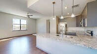 This well-appointed 2-bedroom, 1-bathroom single-floor residence offers a thoughtfully designed open-concept layout that seamlessly connects the kitchen, dining, and living areas. The kitchen serves as the centerpiece of the main living space, showcasing a large island with a granite countertop and undermount sink, complemented by sleek gray cabinetry, stainless steel appliances, and stylish pendant lighting. Rich hardwood-style flooring flows throughout the home, adding warmth and continuity to each room. Ceiling fans are installed in the living area and bedrooms, enhancing comfort year-round. The spacious primary bedroom receives generous natural light through large windows offering outdoor views, and includes a well-organized closet with built-in shelving. The second bedroom is equally bright, with its own window and ample space. A dedicated pantry and laundry area add practical storage and utility. The full bathroom is finished with large-format marble-look tile on both the floors and walls, a soaking tub with shower, a gray double vanity with a white countertop, and an illuminated mirror, creating a clean, spa-like atmosphere. Additional closets and a hallway complete this efficiently planned and modern residence.