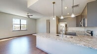This well-appointed 2-bedroom, 1-bathroom single-floor residence offers a thoughtfully designed open-concept layout that seamlessly connects the kitchen, dining, and living areas. The kitchen serves as the centerpiece of the main living space, showcasing a large island with a granite countertop and undermount sink, complemented by sleek gray cabinetry, stainless steel appliances, and stylish pendant lighting. Rich hardwood-style flooring flows throughout the home, adding warmth and continuity to each room. Ceiling fans are installed in the living area and bedrooms, enhancing comfort year-round. The spacious primary bedroom receives generous natural light through large windows offering outdoor views, and includes a well-organized closet with built-in shelving. The second bedroom is equally bright, with its own window and ample space. A dedicated pantry and laundry area add practical storage and utility. The full bathroom is finished with large-format marble-look tile on both the floors and walls, a soaking tub with shower, a gray double vanity with a white countertop, and an illuminated mirror, creating a clean, spa-like atmosphere. Additional closets and a hallway complete this efficiently planned and modern residence.