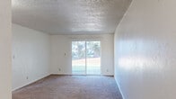 Located at 1550 Q St in Springfield, Oregon, this single-floor, one-bedroom, one-bathroom unit offers a straightforward and functional layout across a compact but well-utilized footprint. The living area is the heart of the space, featuring neutral carpet flooring, white walls, and a textured ceiling that adds visual character. A sliding glass door fills the room with natural light and provides a view of the surrounding greenery, creating a bright and open feel. Adjacent to the living area, the kitchen is equipped with dark wood cabinetry, a white refrigerator, an electric range, and a window that brings in additional daylight. Durable wood-style flooring in the kitchen contrasts with the carpeted living spaces, and a wall-mounted ventilation unit adds to the room's utility. The bedroom is a comfortable, well-proportioned space with plush carpet, a window overlooking the neighborhood, and a reach-in closet with a hanging rod offering practical storage. The bathroom features a full-size soaking tub with a shower, enclosed with clean white surround panels and chrome fixtures. A hallway connects the rooms, contributing to the efficient flow of the overall layout. The unit presents a clean, move-in-ready environment suitable for a variety of living needs.