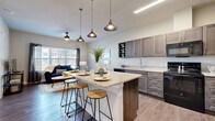 This thoughtfully laid-out one-bedroom, one-bathroom unit offers a functional and stylish living experience across a single floor. The open-concept kitchen and living area serves as the heart of the space, creating a seamless flow between cooking, dining, and relaxing. The kitchen is appointed with taupe shaker-style cabinetry, granite countertops, a central island with bar seating, and black appliances including a range, microwave, dishwasher, and refrigerator. A trio of pendant lights overhead adds a contemporary design touch. The adjacent living area benefits from large windows that invite abundant natural light, with a ceiling fan adding comfort. Wood-style flooring runs throughout the main living spaces, adding warmth and continuity. The bedroom is a comfortable retreat, featuring natural light from a window, wood-style flooring, and access to a dedicated closet. The bathroom is cleanly finished with granite countertops, taupe cabinetry matching the kitchen, a tub and shower combination, and wood-style flooring. Throughout the unit, a neutral color palette and consistent finishes create a cohesive and inviting atmosphere well-suited for everyday living.