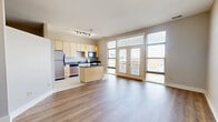 Located at 4462 Glengarry Dr in Beavercreek, Ohio, this single-floor unit offers a thoughtfully designed layout that maximizes its compact footprint. The open-concept kitchen and living area serves as the heart of the space, featuring light maple cabinetry, dark granite countertops, and a full suite of stainless steel appliances including a refrigerator, range, and microwave. A central kitchen island with a matching granite surface provides additional prep and dining space. Track lighting and amber pendant lights overhead lend the kitchen a warm, modern character. Large windows along the living area admit generous natural light and offer views to an outdoor balcony, creating a bright and airy atmosphere. The transition between tile flooring in the kitchen and warm hardwood-style flooring in the living and bedroom areas adds visual interest. The bedroom is a calm, neutral space with the same warm flooring, a large window, and clean white walls. The full bathroom features tile flooring, a combined tub and shower unit, and light wood vanity cabinetry, maintaining a clean and functional aesthetic throughout. The unit's neutral color palette and modern finishes contribute to a cohesive, move-in-ready feel.