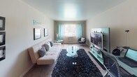 This single-story RiverStone residence offers a practical and well-organized layout that flows from a welcoming living area through to the kitchen and bathroom. The living room is carpeted and generously proportioned, providing ample space for seating and entertainment. A window dressed with light teal curtains allows natural light to filter in, brightening the neutral-toned walls. A wall-mounted air conditioning unit ensures year-round comfort, while framed artwork and decorative accents contribute to a polished, move-in-ready aesthetic.

The layout transitions seamlessly into the kitchen, which features light wood cabinetry, dark granite-style countertops, and black appliances including a gas range, dishwasher, and under-cabinet range hood. The warm hardwood-style flooring in this area adds visual contrast to the carpeted living space and extends down the hallway toward the entryway, where a set of bifold closet doors provides convenient storage.

The bathroom is clean and functional, equipped with a full-size soaking tub and shower combination finished in white, chrome fixtures, and a light blue shower curtain. A mirrored medicine cabinet with built-in shelving adds practical storage. Overall, the space presents a cohesive, comfortable environment with a neutral palette and thoughtful use of available space.