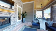 This single-story community space at Brighter 360 combines thoughtful design with inviting, light-filled interiors. The covered outdoor porch sets an impressive first impression, featuring stacked stone accent walls, wood-paneled ceilings, a ceiling fan, and light hardwood flooring. Wicker seating with navy cushions and decorative area rugs create a welcoming atmosphere, while open sightlines extend to the surrounding neighborhood.

Inside, the open-plan lounge and dining area is defined by vaulted ceilings, recessed lighting, and large windows that draw in abundant natural light. A dramatic stacked stone fireplace serves as a focal point in the lounge, flanked by neutral-toned seating arrangements and accented by teal walls. A statement chandelier adds a refined touch overhead.

The dining area features a round wood table with upholstered white chairs, set atop a patterned area carpet. Distinctive wall-mounted planters display cascading succulents and greenery, adding a lively organic element to the space. Interior windows connect zones visually, enhancing the sense of openness throughout.

Select windows frame direct views of an outdoor swimming pool surrounded by mature trees, reinforcing the connection between indoor comfort and outdoor amenity.