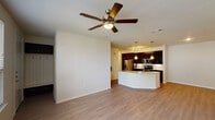 This one-bedroom, one-bathroom apartment in Conroe, TX offers a thoughtfully designed single-story layout that balances modern aesthetics with everyday functionality. The open-concept living and kitchen area is anchored by light wood-style flooring and a ceiling fan, creating a bright and airy atmosphere. The kitchen is a standout feature, showcasing rich dark cabinetry, granite countertops, a classic white subway tile backsplash, and stainless steel appliances including a range, microwave, and refrigerator. A curved peninsula with a sink and pendant lighting serves as both a functional workspace and a natural divider between the kitchen and living area. The living space is generously proportioned, offering ample room for comfortable furnishings, and benefits from natural light through multiple windows. The bedroom is carpeted for warmth and comfort, features a ceiling fan, a door leading to an outdoor balcony, and a spacious walk-in closet with built-in shelving. The full bathroom is well-appointed with dark cabinetry, dual granite-topped vanities, a large mirror, and a glass-enclosed tile shower. The overall design presents a clean, contemporary feel throughout.