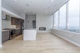 This single-floor high-rise unit showcases a contemporary design with a thoughtfully open layout. The living and kitchen areas share a generous, light-filled space anchored by large floor-to-ceiling windows that frame sweeping urban skyline views. Light hardwood flooring flows throughout the main living area, lending warmth to the modern aesthetic.

The kitchen is a standout feature, equipped with dark wood cabinetry, a subway tile backsplash, stainless steel appliances including a gas range and French door refrigerator, and a sleek wall-mounted range hood. A central island with a white quartz countertop and undermount sink provides both functional workspace and a natural gathering point.

The bedrooms are carpeted for comfort and feature generous proportions, ceiling fans, and large windows that continue the urban views established throughout the unit. The primary bedroom includes direct access to a walk-in closet with built-in shelving and an en-suite bathroom. The bathroom features large-format tile flooring, a floating wood vanity with white countertop, an undermount sink, and a backlit mirror. A second bathroom mirrors this refined, minimalist aesthetic. Overall, the unit presents a clean, neutral palette with consistent modern finishes throughout.