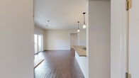 This single-floor residence offers a thoughtfully designed open-concept layout that seamlessly connects the kitchen and living areas. Rich hardwood flooring runs throughout the main living spaces, creating a warm and cohesive aesthetic. The kitchen is a functional centerpiece, featuring granite countertops, rich medium-toned wood cabinetry, black appliances including a range and microwave, and a spacious peninsula with an undermount sink. Elegant pendant lighting above the peninsula adds a refined touch, while a dedicated laundry area with a full-size washer and dryer is conveniently accessible nearby. The living area is bright and open, benefiting from natural light provided by sliding glass doors that lead to an outdoor space. The bedrooms are carpeted for comfort and are generously sized, with ample closet space including a large walk-in closet outfitted with wire shelving and hanging rods, as well as an additional standard closet. The bathroom features warm wood cabinetry, a granite-topped vanity with an integrated sink, a large mirror, and hardwood-style flooring. Neutral, warm-toned walls throughout the residence create a welcoming atmosphere that complements the natural materials used across the space.