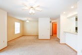 This single-floor residence offers a well-organized layout designed for comfortable everyday living. The kitchen is equipped with white cabinetry trimmed in warm wood tones, light countertops, a stainless steel sink, and a full suite of appliances including a refrigerator, electric range, built-in microwave, and dishwasher. A pass-through counter opens the kitchen to the carpeted living area, which features recessed lighting and a ceiling fan, creating a bright and connected common space. The living room includes a sliding glass door with vertical blinds, allowing natural light to filter in and providing outdoor access. Multiple bedrooms are present throughout the unit, each finished with plush carpet, ceiling fans, and natural light from windows. The bedrooms offer closet space and a calm, neutral color palette. The bathroom is tiled with earthy stone-look flooring and includes a full soaking tub with a shower rod. A standout feature is the in-unit laundry closet, which houses a full-size washer and dryer behind bifold doors. Throughout the space, warm wood door and trim accents complement the neutral walls, creating a cohesive and practical living environment.