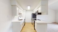 This single-floor residence offers a bright, well-maintained layout designed for comfortable everyday living. The standout feature is the galley-style kitchen, which has been thoughtfully updated with crisp white shaker cabinetry, white subway tile backsplash, light quartz countertops, and a full suite of stainless steel appliances including a refrigerator, range, microwave, and dishwasher. Light hardwood-style flooring runs throughout the kitchen, adding warmth to the clean, neutral palette. The open living area is generously proportioned, featuring vaulted ceilings that lend a sense of airiness to the space. A peninsula counter connects the kitchen to the living area, providing a casual dining or serving surface. Soft, neutral carpet covers the living and bedroom areas, contributing to a cozy atmosphere. The bedroom is a comfortable, well-sized room with a ceiling fan, natural light from a window with blinds, and the same plush carpeting. The bathroom is clean and functional, featuring a full tiled tub-and-shower combination in crisp white. Throughout the space, a consistent neutral color scheme, white walls, and ample lighting create a bright, move-in-ready environment that is both practical and easy to personalize.
