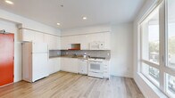 This efficiently designed 1-bedroom, 1-bathroom unit offers a thoughtfully arranged single-level floor plan that maximizes every square foot. Light-toned hardwood-style flooring runs throughout, lending a cohesive and airy feel to the entire space.

The kitchen is a standout feature, showcasing sleek white cabinetry extending to the ceiling for ample storage, complemented by a stylish mosaic tile backsplash in neutral tones. Warm-hued countertops provide a functional workspace, while white appliances — including a refrigerator, dishwasher, oven/range, and over-the-range microwave — complete the setup. Recessed lighting brightens the area effectively.

The living area flows directly from the kitchen, benefiting from a large window that invites natural light and frames an exterior view. The open layout creates a comfortable and versatile space.

The bedroom is a quiet, well-proportioned room finished in crisp white walls and the same light flooring. A sliding door leads to a built-in closet, offering convenient storage.

The bathroom features a full-size soaking tub with an overhead shower and curtain rod, a toilet, and a vanity, all set against clean white walls and matching flooring, creating a simple yet functional space.

Overall, the unit presents a bright, modern aesthetic with a clean, minimalist design sensibility.