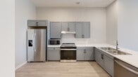 Located at 608 2nd Ave S in the heart of downtown Minneapolis, this one-bedroom, one-bathroom unit offers a thoughtfully designed layout that maximizes every square foot. Light-toned luxury vinyl plank flooring runs throughout, creating a cohesive and modern aesthetic across all rooms.

The kitchen is well-appointed with grey shaker-style cabinetry, white quartz countertops, a subway tile backsplash, and a full suite of stainless steel appliances including a French door refrigerator, electric range, and built-in microwave. A sink with ample counter space completes this functional cooking area.

The bedroom is a comfortable retreat featuring a large window that frames captivating views of the Minneapolis downtown skyline, allowing natural light to fill the room. Its neutral wall tones and clean lines contribute to a calm, restful atmosphere.

The bathroom is generously proportioned and designed with accessibility in mind, featuring a walk-in shower with grab bars, matte black hardware accents, and light wood-look flooring. Conveniently adjacent to the bathroom is a dedicated laundry area with a full-size Whirlpool washer and dryer.

The entryway features a solid wood-toned door with a modern smart lock, opening into a bright, open living space. Clean wall finishes and a neutral palette throughout give this unit a fresh, move-in-ready appeal.
