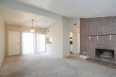 This single-floor residence offers a well-organized layout that balances comfort and functionality throughout. The centerpiece of the living area is a striking full-wall brick fireplace with a gold-framed insert, adding warmth and character to the space. Plush wall-to-wall carpeting extends across the living area, which is bathed in natural light streaming through a large sliding glass door that opens to a private balcony overlooking lush greenery. A ceiling fan overhead provides year-round comfort, while a textured ceiling adds subtle architectural detail throughout the home. The kitchen is efficiently designed with warm oak cabinetry, ample counter space, and white appliances including a dishwasher, range, and refrigerator, all set on easy-care tile flooring. The bedroom is a quiet, carpeted retreat with a dedicated window that invites natural light. Two bathrooms serve the home, each featuring oak vanity cabinetry, a white countertop with an integrated sink, and a large wall mirror. One bathroom includes a shower with a decorative curtain and tile flooring. Neutral wall tones and consistent finishes throughout the home create a cohesive, move-in ready atmosphere that is both practical and inviting.