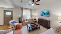 This two-story residence offers a well-organized layout across both levels, combining practical design with comfortable living spaces. The main level features warm hardwood flooring throughout the open living and dining areas. The living room is generously sized, accommodating multiple seating arrangements beneath a ceiling fan, and flows naturally toward a staircase with wood-railed banisters leading to the upper floor. The adjacent dining area benefits from natural light through a large window and is highlighted by a chandelier overhead.

The kitchen is equipped with dark wood cabinetry, granite countertops, a breakfast bar peninsula, and a full suite of stainless steel appliances including a refrigerator, range, and built-in microwave. A dedicated laundry area with a full-size washer and dryer adds everyday convenience.

Upstairs, the bedrooms feature plush carpet and ceiling fans. The primary bedroom showcases vaulted ceilings and access to a walk-in closet with wire shelving. A secondary bedroom receives natural light through a window with decorative curtains. Bathrooms include tile flooring, a tub-shower combination, and vanity storage.