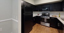 This single-floor residence offers a cohesive and well-designed layout across multiple rooms, united by a calm, neutral color palette of soft grey-green tones and crisp white trim. The kitchen is outfitted with dark espresso cabinetry, white countertops, and stainless steel appliances, including a gas range and built-in microwave, complemented by wood-look flooring that adds warmth. A dedicated dining nook adjacent to the main living area features chair-rail molding and overhead lighting, creating an intimate setting for meals. The living room is anchored by sliding glass doors that offer views to an outdoor space and allow natural light to fill the room, finished with hardwood-style flooring and crown molding. Two well-proportioned bedrooms feature plush carpeting, natural light from oversized windows, and closet storage. Both bathrooms mirror the kitchen's dark vanity cabinetry paired with white countertops and light stone-look tile flooring; one bathroom includes a tub-shower combination, while the other offers a bright, open layout. The overall design is clean, functional, and consistent throughout.