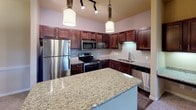 Located at 650 Leora Ln in Lewisville, TX, this single-story residence offers a thoughtfully designed layout with a cohesive blend of finishes throughout. The kitchen serves as a functional centerpiece, showcasing rich dark wood cabinetry, granite countertops, a full suite of stainless steel appliances including a refrigerator, electric range, and built-in microwave, as well as a glass tile backsplash and pendant lighting overhead. A large island provides additional prep space and adds to the open, inviting feel of the area.

The living and hallway areas feature plush carpeting that extends into the bedrooms, each of which is fitted with ceiling fans and windows dressed with blinds that allow for natural light. The open hallway connects the living space seamlessly to the private areas of the home.

The bathrooms are finished with dark wood vanities, granite countertops, framed mirrors, and full tub-shower combinations with tiled surrounds. Rich wood-look flooring anchors the bathrooms, complementing the warm, neutral tones found throughout the home.

Overall, the space presents a clean, well-maintained interior with consistent finishes, practical storage solutions, and a layout designed for comfortable everyday living.