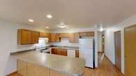 This single-story unit on Ernie Drive in Elwood, Indiana offers a well-designed, open-concept layout with consistent finishes throughout. The kitchen serves as a central hub of the space, featuring warm honey-toned oak cabinetry extending to the ceiling for ample storage, granite-style countertops, and white appliances including an electric range, dishwasher, and full-size refrigerator. A peninsula counter extends outward, providing additional prep space and a natural transition into the open living and dining areas. Recessed lighting illuminates the kitchen, while flush-mount fixtures carry through the rest of the unit.

The living and dining areas are bathed in natural light from large windows and feature light hardwood-style flooring with warm-toned baseboards. A ceiling fan with integrated lighting adds functionality to the living area, which is further enhanced by a pendant light fixture in the dining zone. Interior doors with wood-trimmed frames connect to additional rooms, including carpeted bedrooms with windows that invite natural light.

Two full bathrooms are included, each featuring a wood-vanity with an integrated sink, lighted mirror, tile flooring, and a walk-in shower or tub surround. The overall aesthetic is clean, practical, and move-in ready.