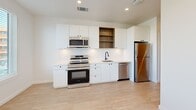 Located at 900 Hangar Dr in Oklahoma City, OK, this well-designed one-bedroom, one-bathroom unit offers a thoughtful layout across a single floor. The open kitchen is a standout feature, showcasing crisp white cabinetry with matte black hardware, warm wood open shelving, a white tile backsplash, light hardwood-style flooring, and a full suite of stainless steel appliances including a range, microwave, dishwasher, and refrigerator. The kitchen flows naturally into the living area, creating an open and functional space. The bedroom is carpeted for comfort and features a ceiling fan with light, neutral walls, and a built-in closet with double hanging rods and shelving — offering practical storage. The bathroom is finished with large-format grey floor tiles, a white tub and shower combination with matte black fixtures, a toilet, and a vanity with a bold navy blue cabinet base and white countertop. Recessed lighting and a ventilation vent complete the clean, modern aesthetic. Overall, the unit presents a cohesive contemporary design with quality finishes throughout, making efficient use of its compact footprint.